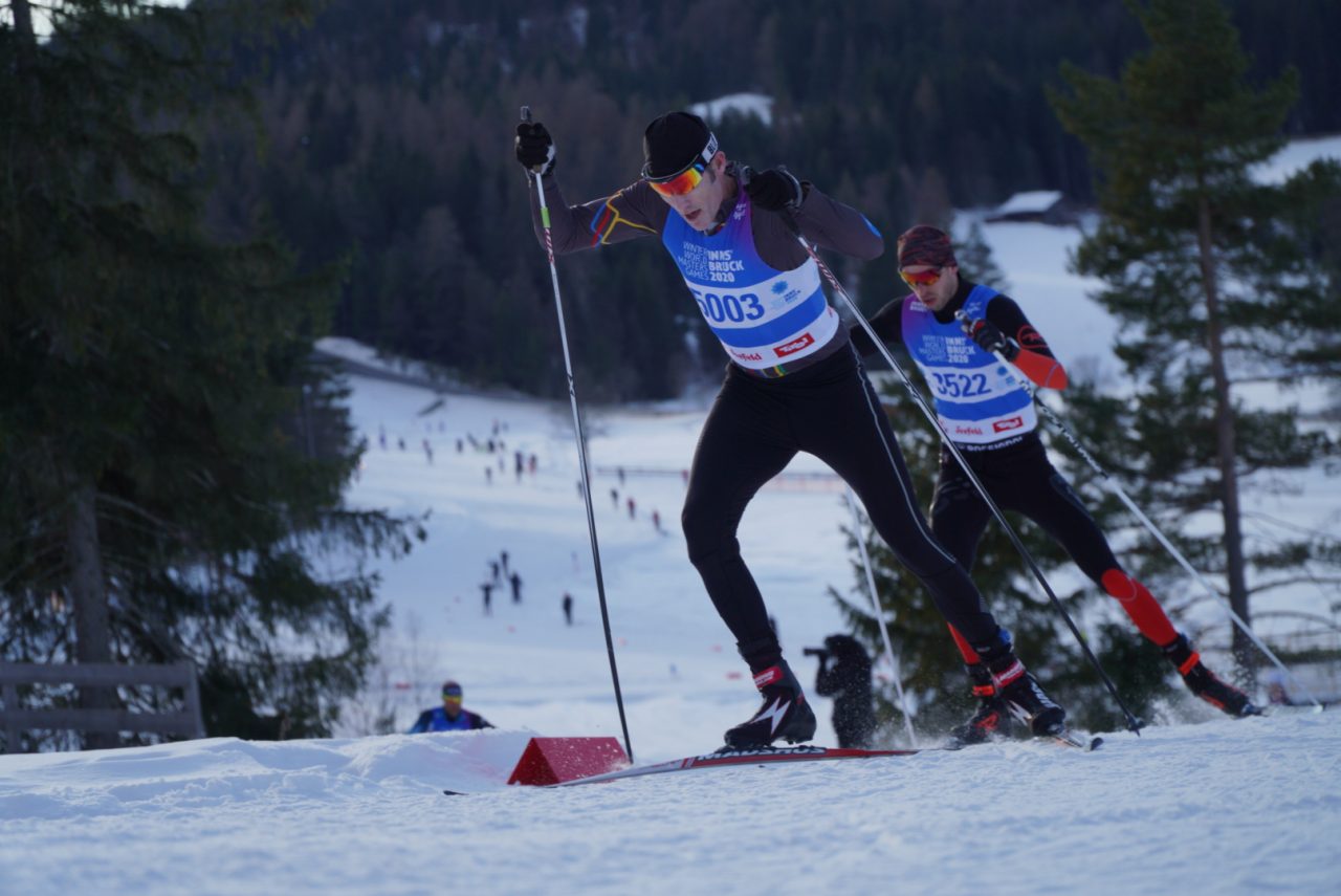 Two masters racers skate up a rise in bibs from the 2020 Winter World Masters Games in Seefeld, Austria