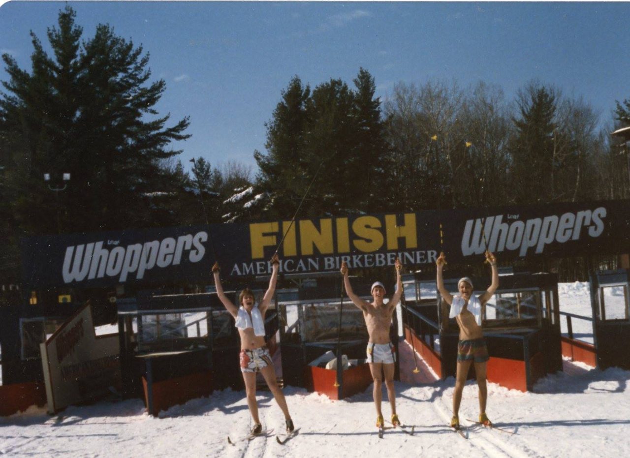 Three skiers in shorts raise their poles under the American Birkebeiner finish banner at Telemark