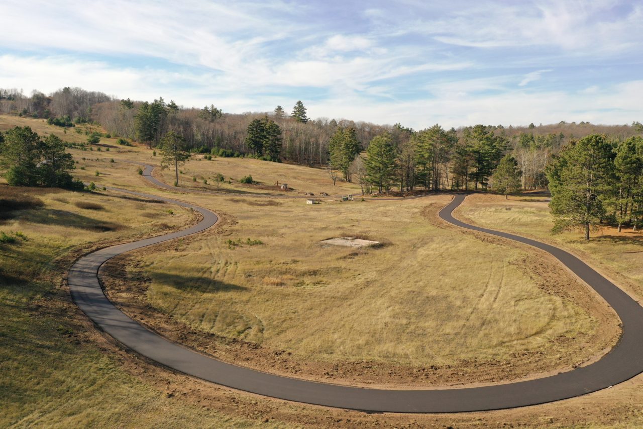 Aerial view of a curving paved rollerski loop winding through dry grass and scattered pines