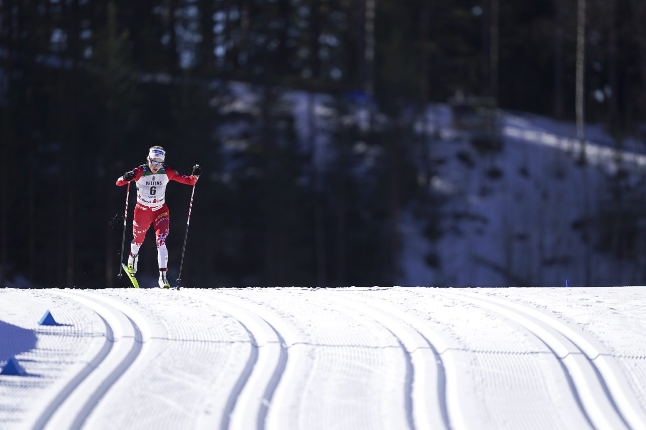Therese Johaug in a red suit skiing alone through classic tracks