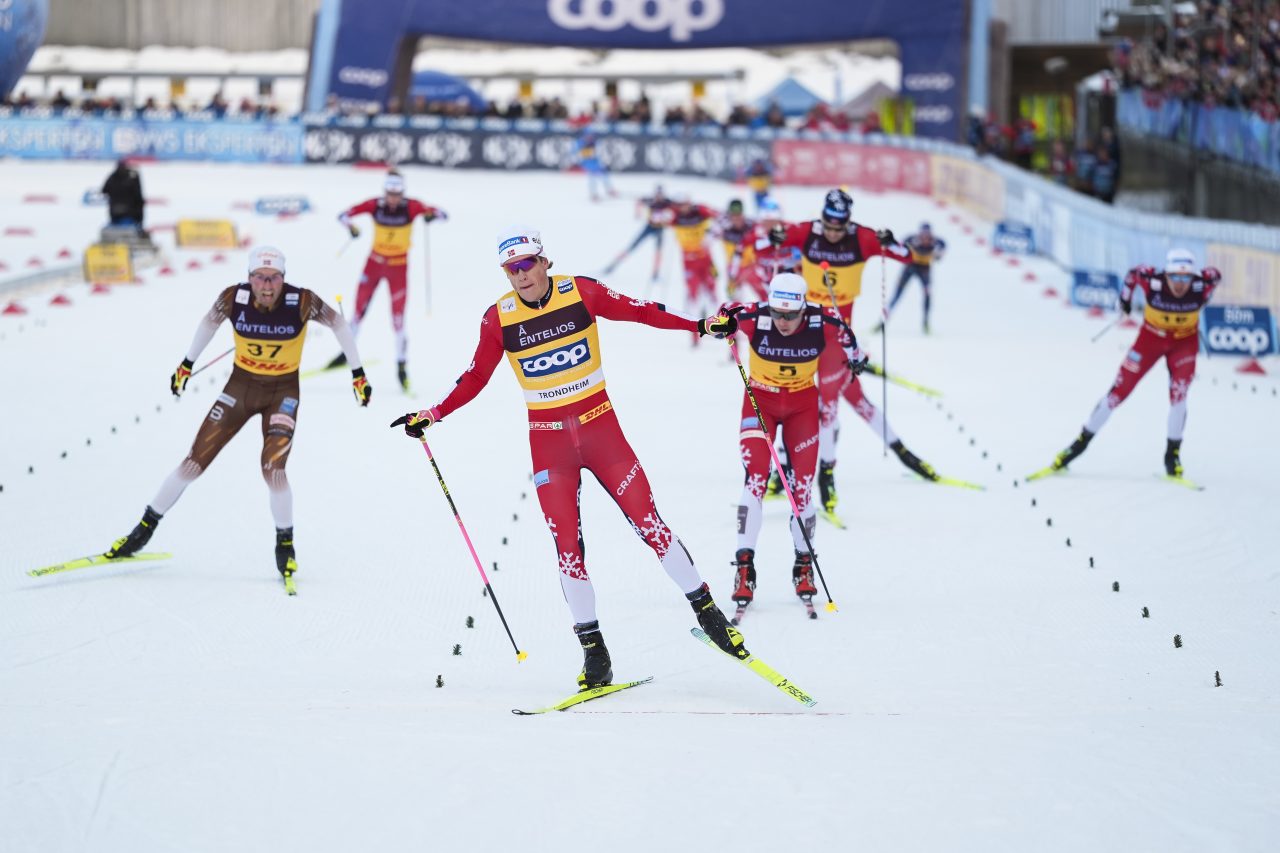 Johannes Høsflot Klæbo in a yellow leader bib skating ahead of several Norwegian teammates in red suits