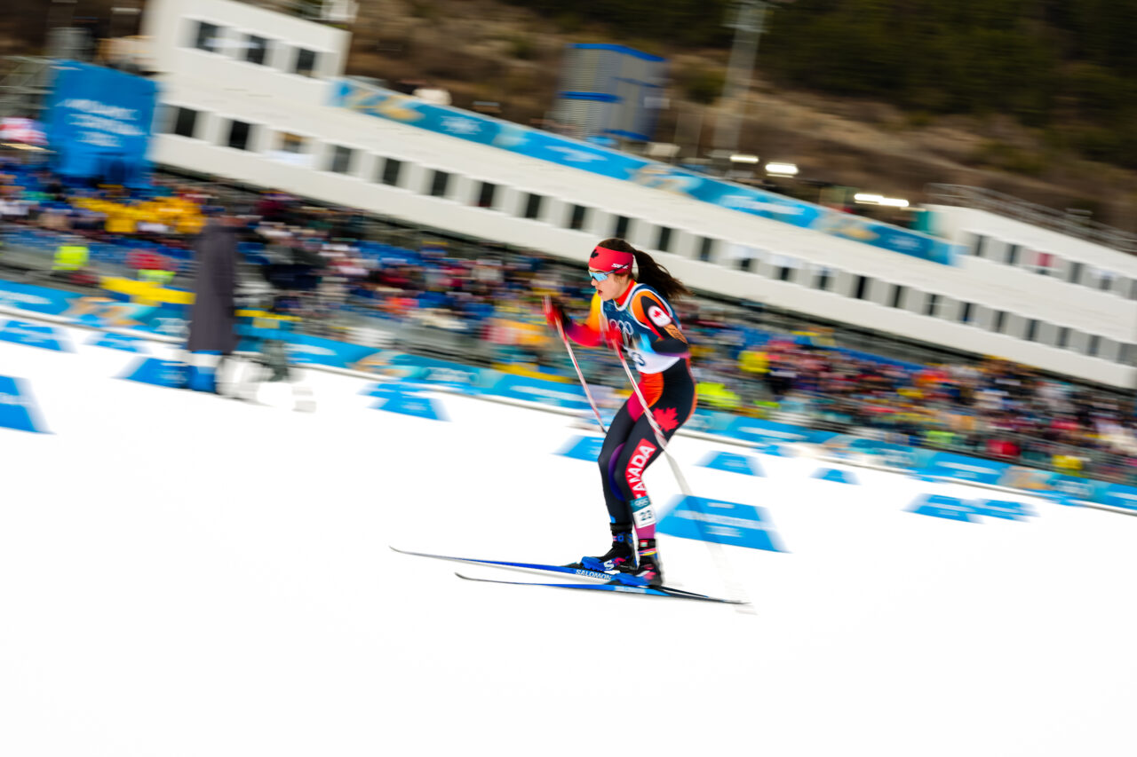 Alison Mackie racing the Olympic 10 k freestyle in Tesero, panned against a packed grandstand.