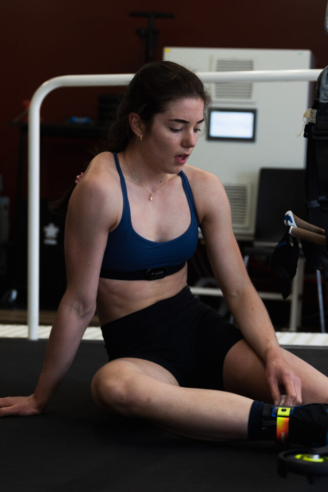 Alison Mackie sitting on a laboratory floor catching her breath and unstrapping a sensor from her leg.