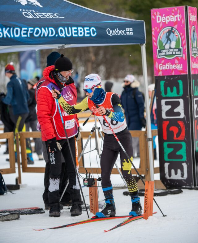 An official in a red jacket steadies a racer in the start gate beneath a Candy Cane Cup banner.