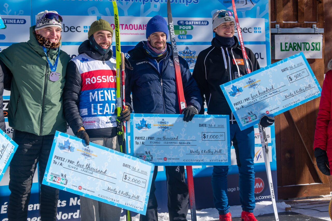 Four skiers holding oversized presentation cheques in front of an Eastern Championships backdrop.