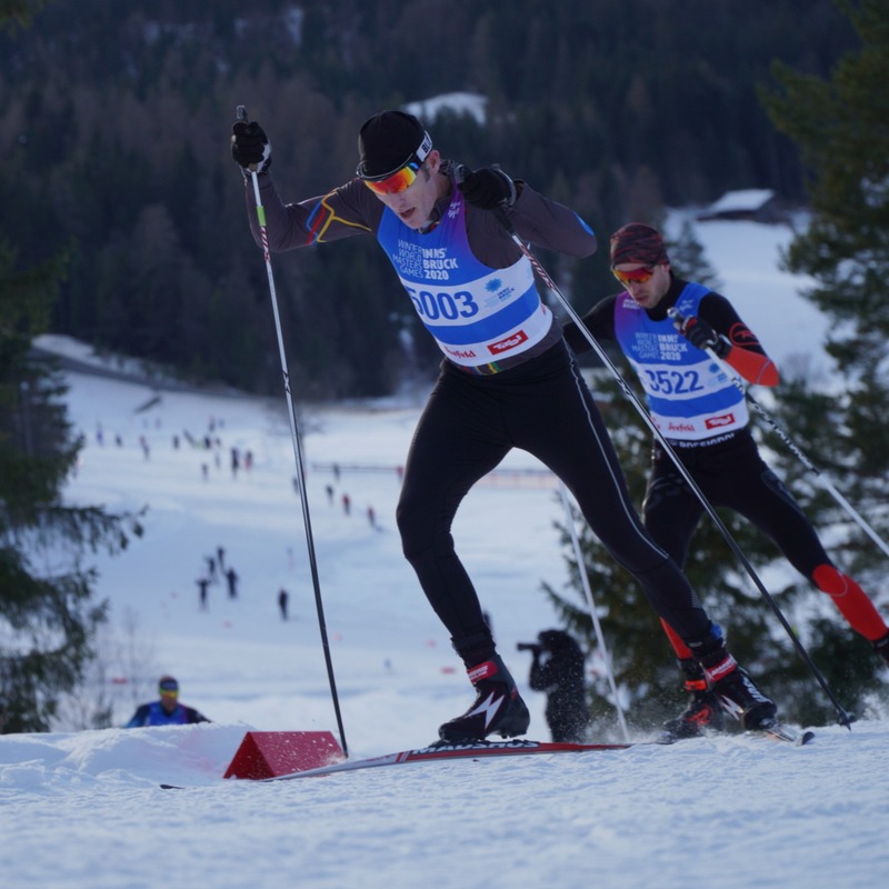 Two masters racers skate up a rise wearing 2020 Winter World Masters Games bibs at Seefeld, Austria