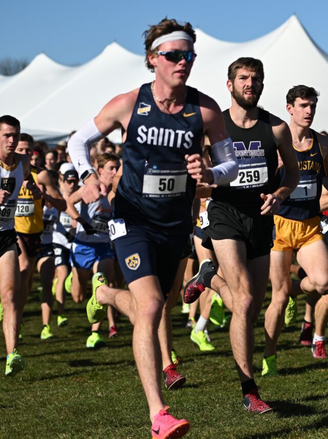 Lars Dewall in a St. Scholastica singlet, headband and sunglasses running at the front of a large field, with white event tents behind.
