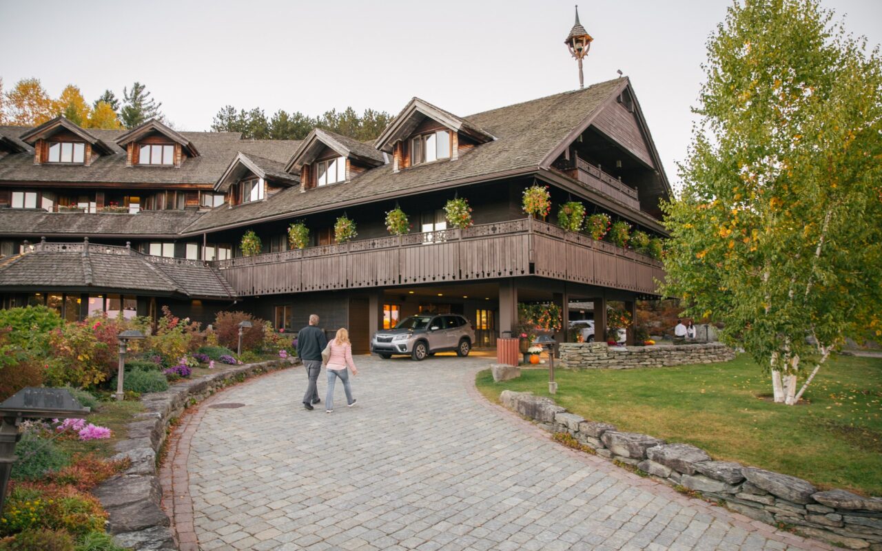 Two guests walk up the curving cobblestone drive toward the wooden Austrian-style main lodge with flower boxes on its balconies